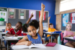 Young girl raising hand in full classroom