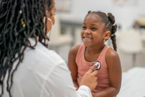 Pediatric nurse listening to heart of young girl