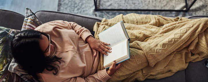 Woman reading book on sofa in blanket