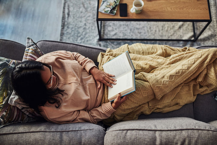 Woman reading book on sofa in blanket