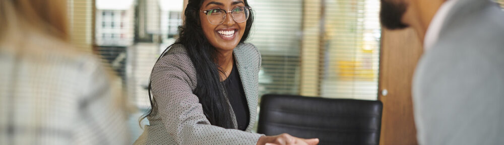 An applicant shaking an interviewer’s hand while the interviewer’s associate greets her before an interview begins. The photo is focused on the applicant.