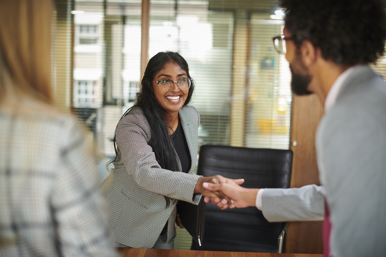 An applicant shaking an interviewer’s hand while the interviewer’s associate greets her before an interview begins. The photo is focused on the applicant.