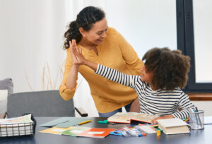 ABA therapist giving a high five to a smiling child during a therapy session, with learning materials on the table
