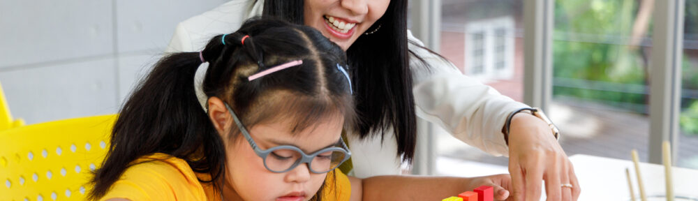 A young girl with disability playing a puzzle toy with her ABA teacher in the classroom.