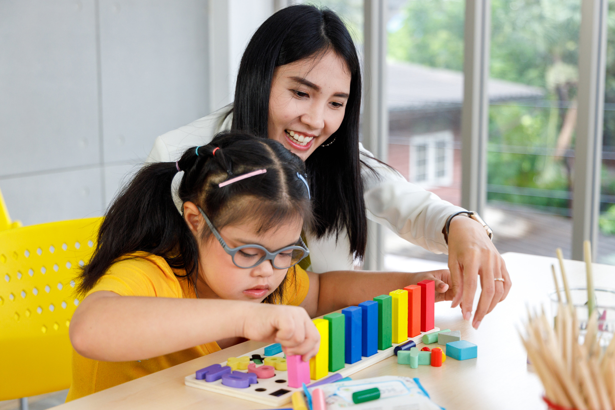 A young girl with disability playing a puzzle toy with her ABA teacher in the classroom.