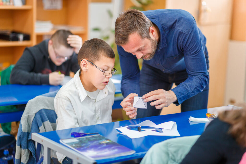 Male special education teacher holding a model made by an intellectually challenged elementary student